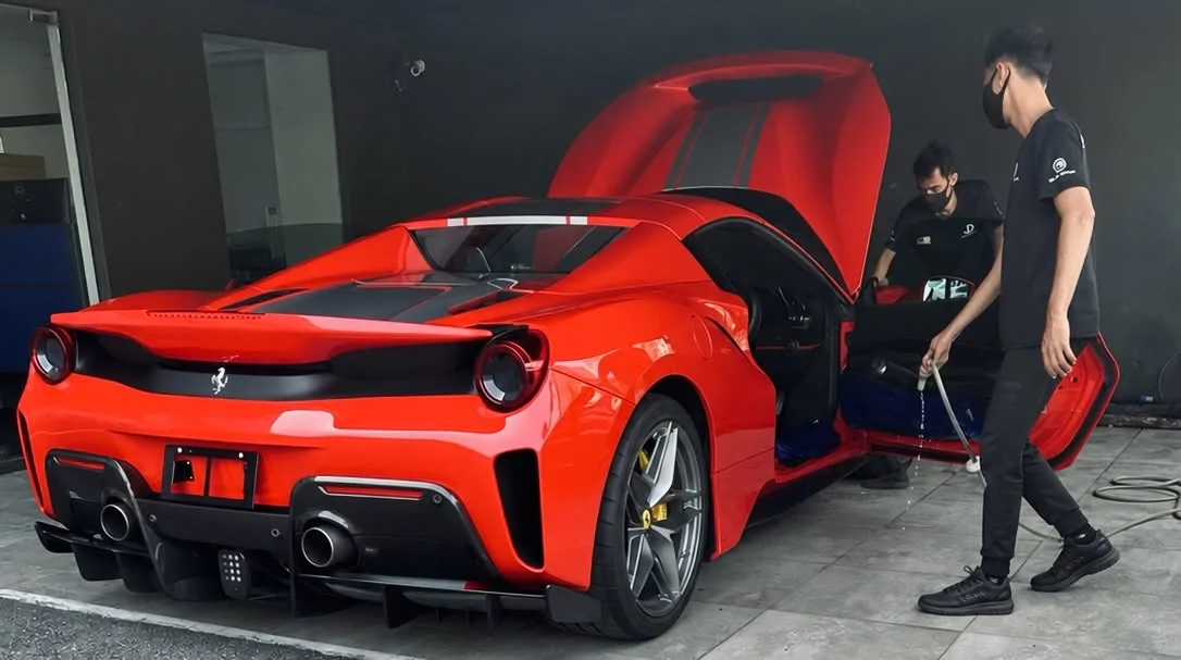 Two people attending to a red sports car with its door open at Jon Detailing