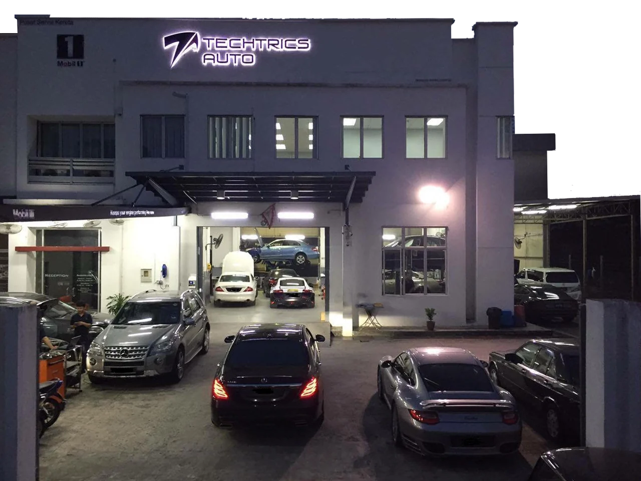 Techtrics Auto’s illuminated workshop frontage, with cars in the forecourt and service bays